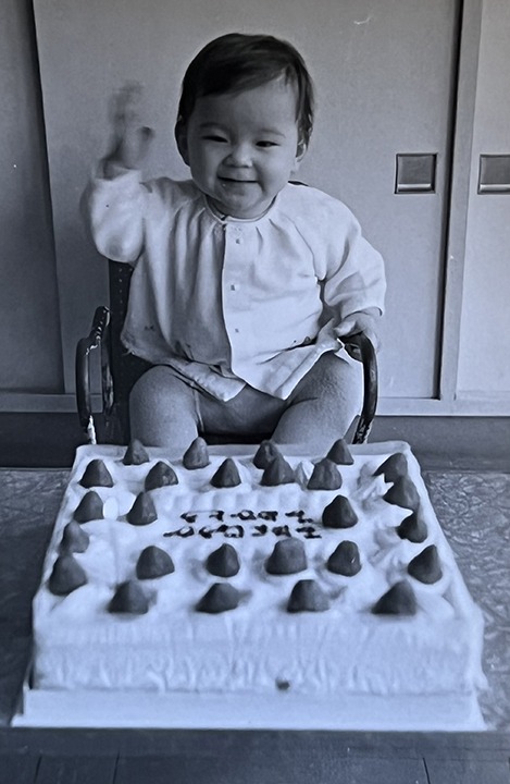 Baby Val in front of a cake. She looks very excited because she is finally getting a snack!